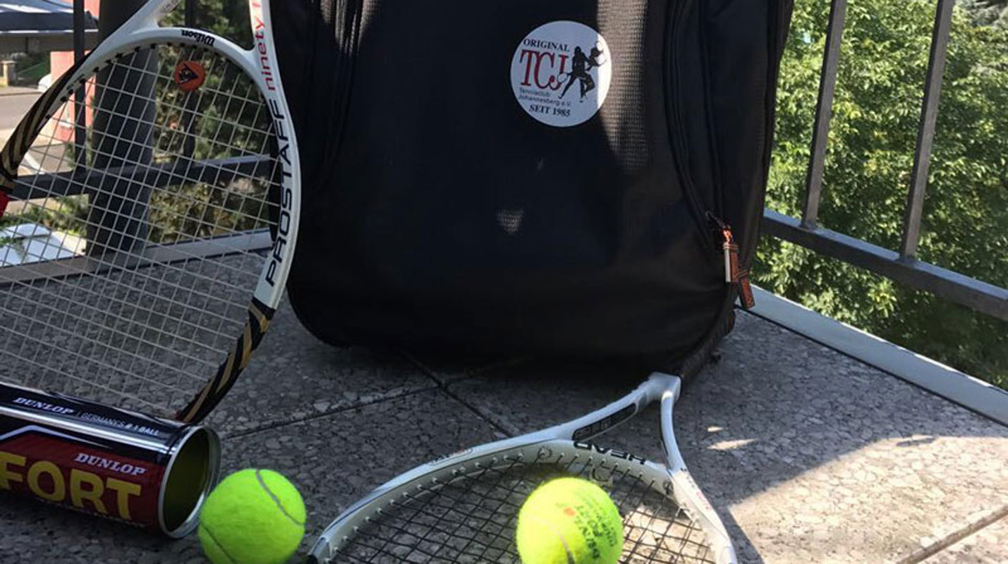 Zwei Tennisschläge mit Tennisbällen vor einem schwarzem Rucksack.